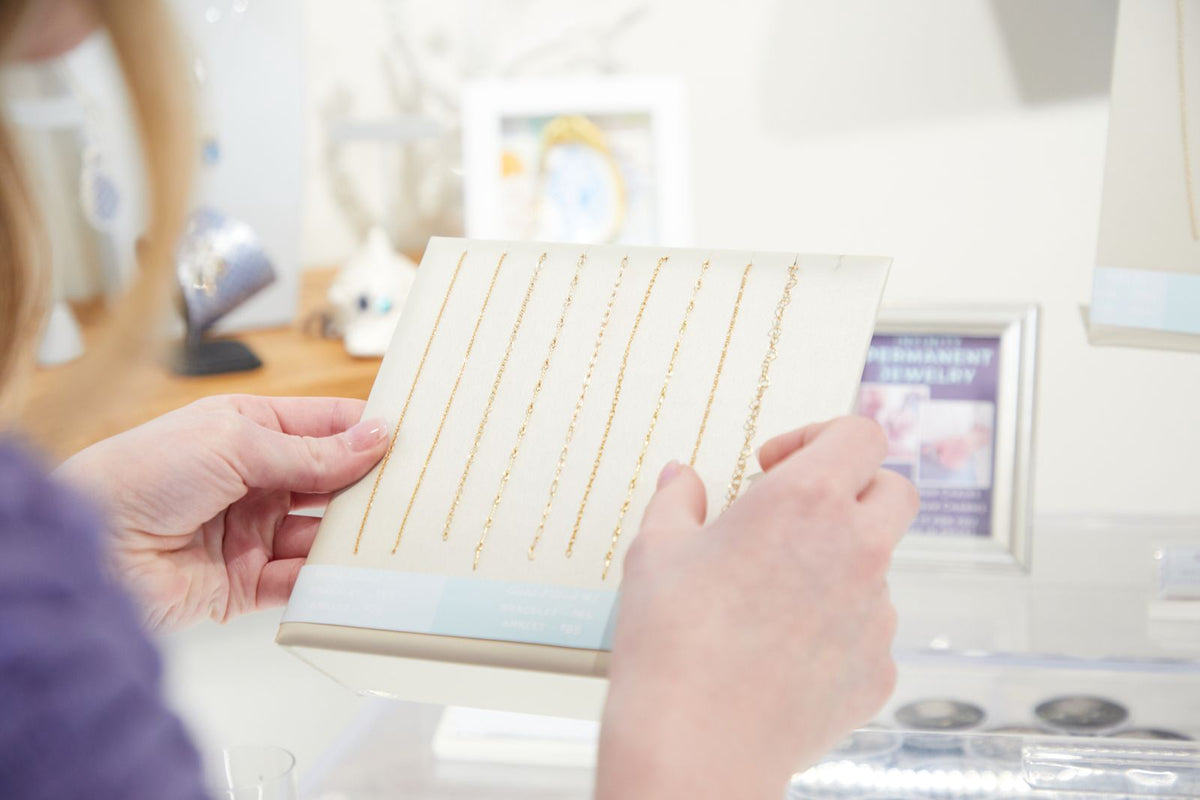 A customer choosing a permanent jewelry chain from the Moonrise display board in the studio