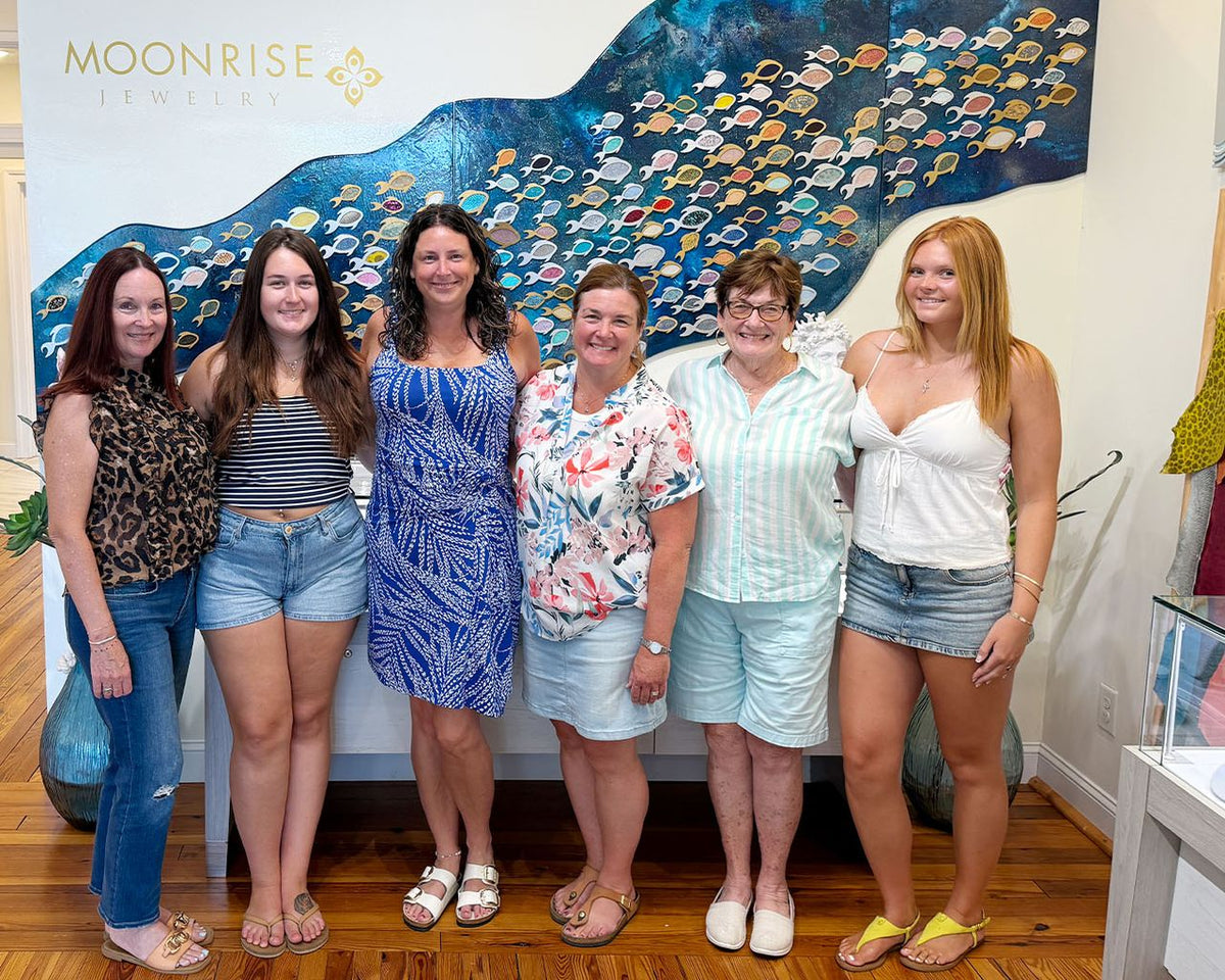 Six family members of different generations together in front of the Moonrise fish mural after their permanent jewelry appointment
