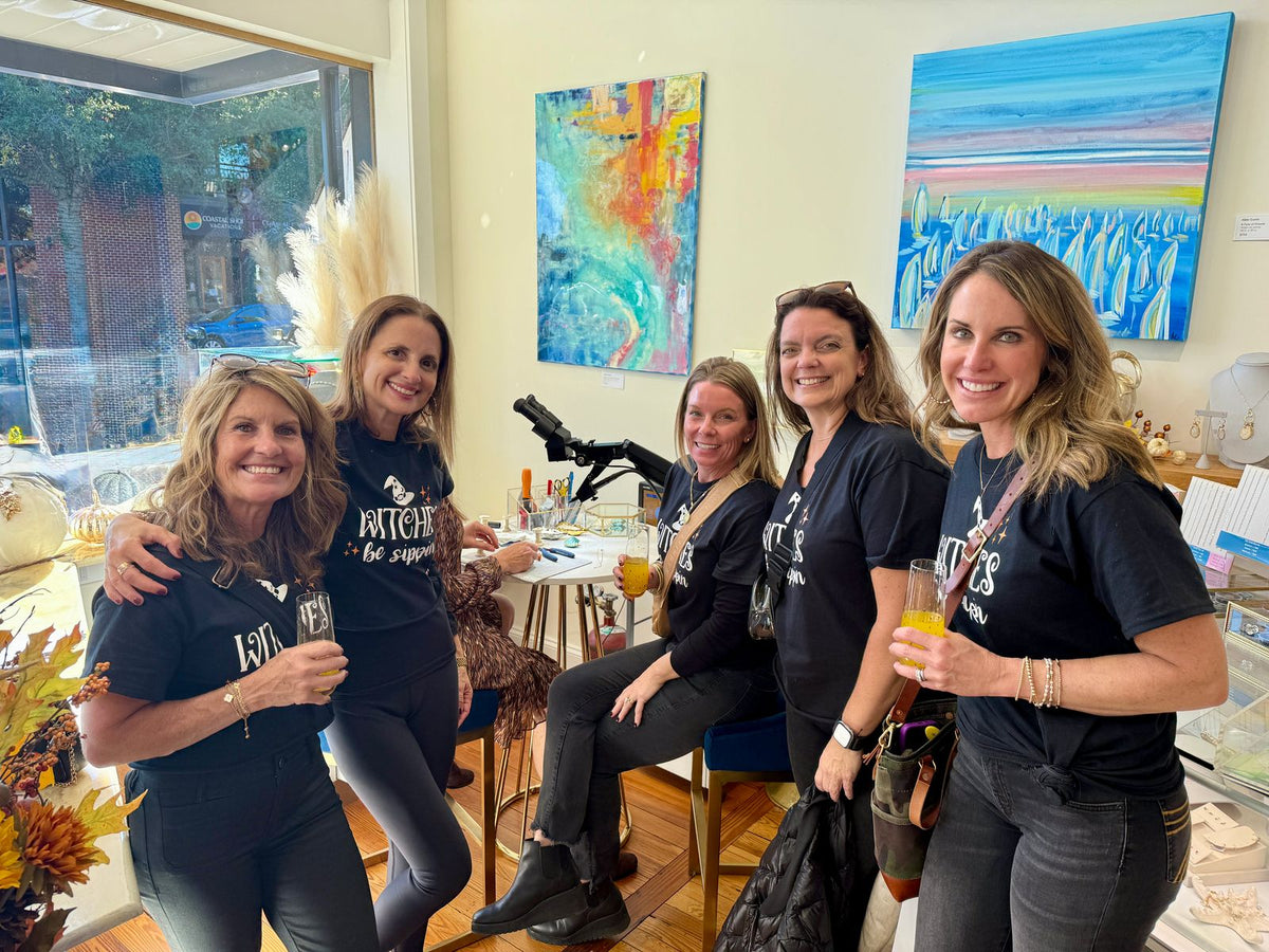A girls trip group in matching shirts raising a toast at the Moonrise permanent jewelry table