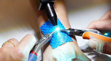 A pulse arc welder joining a permanent jewelry chain with a tiny spark, with a shield protecting the wrist